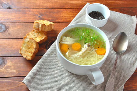 Chicken soup with noodles and vegetables in bowl on wooden background homemade healthy mealの写真素材