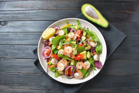 Avocado salad with shrimps, cherry tomatoes, arugula beet leaves, red onion, yellow sweet pepper. Healthy lunch plate  with vegetables and shrimpsの写真素材