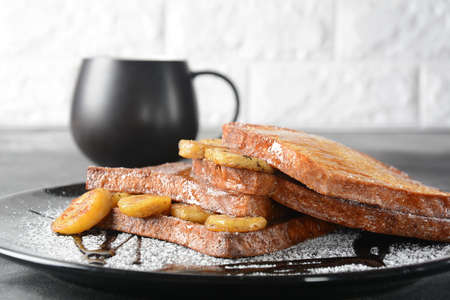 French toasts with fried plantains, dripping maple syrup, sugar powder on a black plate. French...
