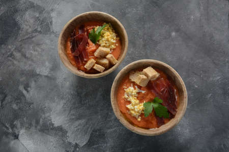 Traditional Spanish andalusian tomato cream soup Salmorejo served with egg, ham jamon, bread in wooden bowl. Summer cold soup conceptの写真素材