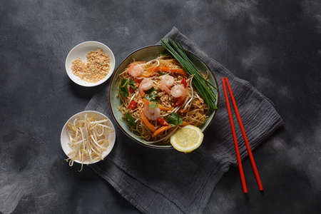 Pad Thai- traditional Thai dish with stir fried rice noodles, shrimps and vegetables on a dark background, copy spaceの写真素材