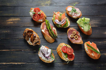 Brushetta or traditional Spanish tapas. Appetizers with Italian antipasti snacks. Variety of small sandwiches with prosciutto, cherry tomatoes, salmon, cream cheese, cucumber, radish, asparagusの写真素材