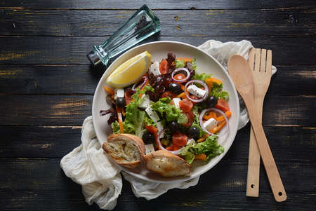 Greek salad with fresh cucumber, cherry tomatoes, sweet pepper, lettuce,red onion, olives and olive oil on dark wooden rustic background . Healthy food conceptの写真素材