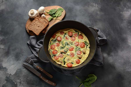 Frittata made of eggs, mushrooms, cherry tomatoes and spinach served in a pan. Italian cuisine.
