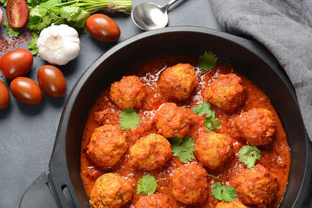 Meatballs in sweet and sour tomato sauce with spices served in a frying pan on dark background . Top...