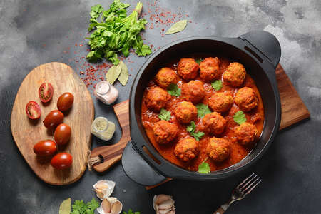 Meatballs in sweet and sour tomato sauce with spices served in a frying pan on dark background . Top...