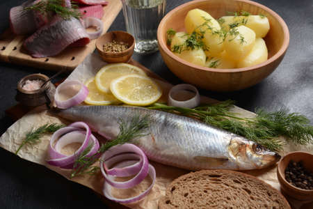 Herring fish  on wooden board  with pepper, herbs, red onion and lemon on black  background. Top view with copy space with potatoes slices and rye breadの写真素材