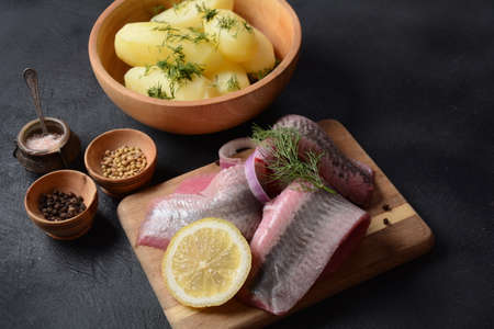 Fillet of Herring fish  on wooden board  with pepper, herbs, red onion and lemon on black  background. Top view with copy space with potatoesの写真素材