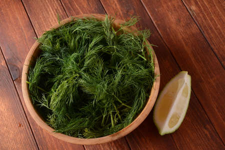 Fresh dill in wooden bowl with lemon on wooden background. Rustic styleの写真素材