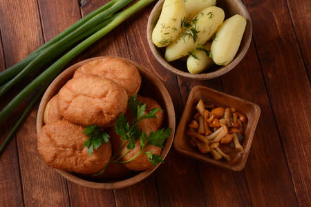 Stuffed Buns (Pirozhki) in wooden bowl on the wooden background. With green onions and Homemade...