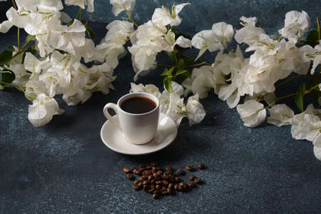 Composition with white cup of coffee , beans  and flowers as backgroundの写真素材