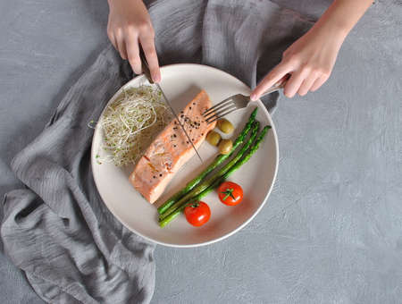 Baked salmon steak with basil and vegetables on a gray background. salmon steak with pepper ready to eat, with a fork and a knife on it. Placed on a white plate with sparrow-grass and tomatoesの写真素材