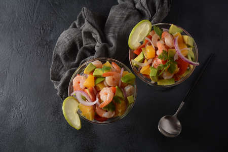 Ceviche salad with shrimps, oranges and avocado in glass bowl on a dark or grey background. Latin American food. Delicious, freshly made shrimp ceviche. Shrimp marinated in lime and orange .の写真素材