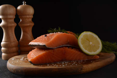 Fresh raw salmon fish fillet with cooking ingredients, herbs and lemon on black background. Keto diet, unsaturated fats, omega 3, healthy nutrition.の写真素材