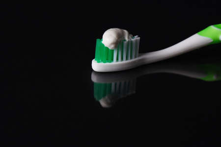 Toothbrush with toothpaste on black background with reflection