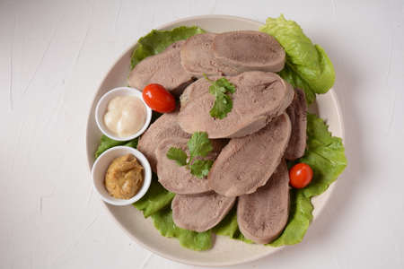 Sliced Beef Tongue Slices on a platter with lettuce leaves, cherry tomatoes and Dijon mustard on a wooden backgroundの写真素材