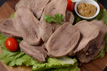 Sliced Beef Tongue Slices on a platter with lettuce leaves, cherry tomatoes and Dijon mustard on a wooden backgroundの写真素材