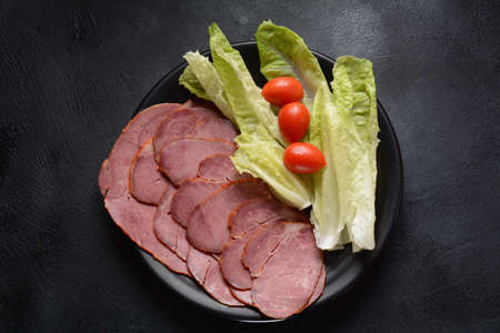 Smoked sliced beef with cherry tomatoes and lettuce on black plateの写真素材