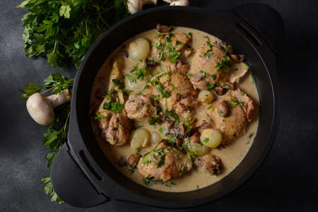 Fricassee - French Cuisine. Chicken stewed in a creamy sauce with mushrooms in a black dutch oven on a black tableの写真素材