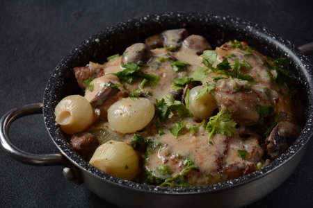 Fricassee - French Cuisine. Chicken stewed in a creamy sauce with mushrooms in casserole pan on a black tableの写真素材