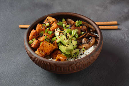 Sweet, spicy , crispy and fried Tofu  in  a  bowl with teriyaki sauce, avocado, fried mushrooms, sesame seeds and rice. Served with green Matcha Tea. Healthy vegan food, gluten-free. Buddha bowlの写真素材