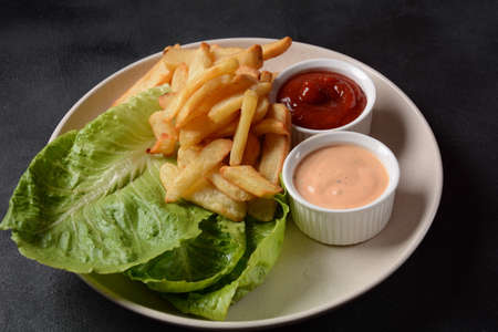 French fries with sauce and lettuce on black background