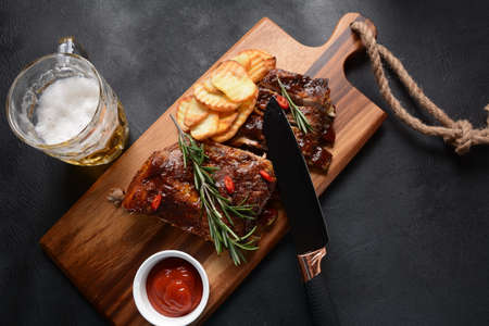Closeup of pork ribs grilled with BBQ sauce and caramelized in honey. Tasty snack to beer on a wooden Board. Grilled pork ribs with knife, spices on a stone backgroundの写真素材