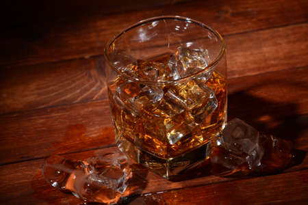 Glass of whisky or whiskey or bourbon on ice  on wood barの写真素材