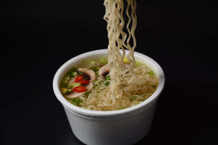 Chopsticks use to pickup tasty noodles in bowl on dark background. Traditional asian meal on a...