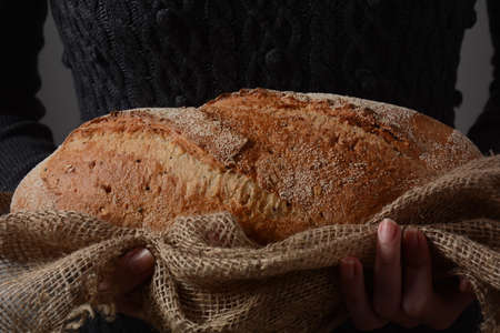 Brown fresh hot Rye bread in a tender girl's hands. Dark wall on a background, rustic photography