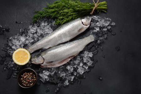 Fresh trout on dark table with lemon, pepper and dill. Tasty fish ready for cooking. Healthy seafood...