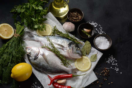 Raw fresh uncooked dorado or sea bream fish with lemon, herbs, oil, vegetables and spices on on...