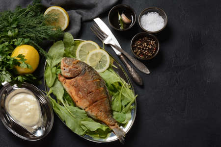 Fried fish dorado with fresh herbs and lemon on silver trayの写真素材