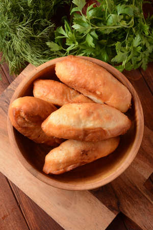Russian Patties (Pasties, Hot Cakes, Pirozhki, Pies) on wooden cupboard . Traditional homemade fried...