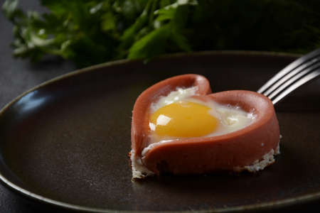 Two sausages in a heart-shaped fried eggs on black plate. Breakfast on Valentine's Day