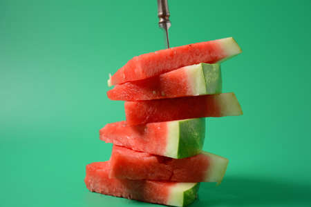 Fresh sliced watermelon pieces on bright background, pierced with a knifeの写真素材