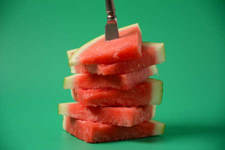 Fresh sliced watermelon pieces on bright background, pierced with a knife