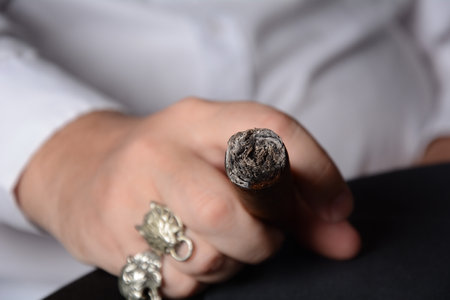 Elegant man wearing white shirt holds a smoking Cuban cigar