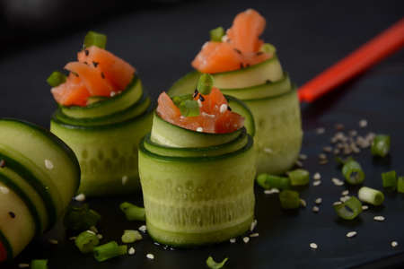 Cucumber rolls with pieces of salted salmon, black and white sesame seeds, chopped green onion....