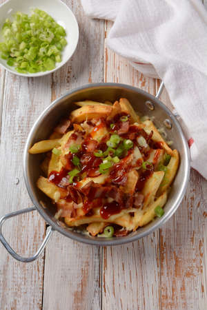 French fries with Melted Cheddar Cheese with Crispy Bacon. Poutine with cheese, bacon and green...