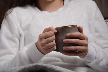 A girl warms her hands with a mug containing hot broth. Autumn concept