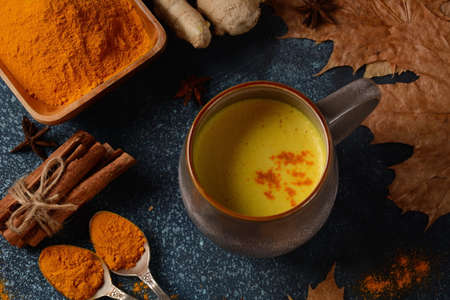 Tasty hot turmeric curcuma milk in cup on  table. Arranged with turmeric powder, cinnamon, anise and spices.の写真素材