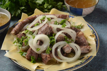 Beshbarmak - National Kazakh dish, prepared with meat and pasta. Beshbarmak dish close-up on a plate on the table. Large pieces of stewed meat and onionの写真素材