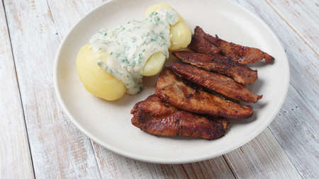 Crispy fried pork with creamy parsley sauce and boiled potato in the plate on the table or stegt...