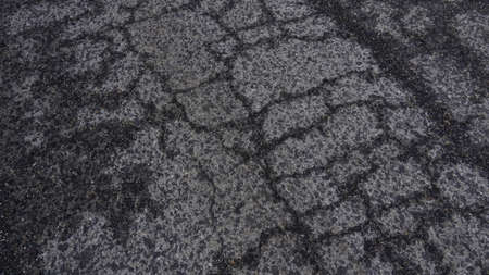 Top view of an old asphalt road in wet cracks. Worn road with cracks texture.
