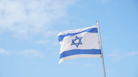 Israeli flag weaving in the wind against bright skiesの写真素材