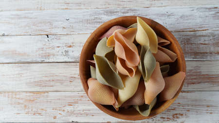 Conchiglie, or colorful shells or seashells in a wooden bawl. A type of Italian pasta