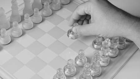 A chessboard with a hand starting to move a chess piece. Clear glass chess figures on a chessboard