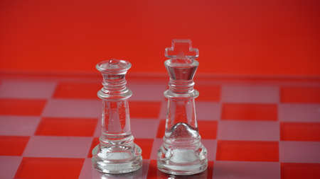 Pieces of transparent chess, king and queen. Transparent chess figures on chessboard, red tone.の写真素材