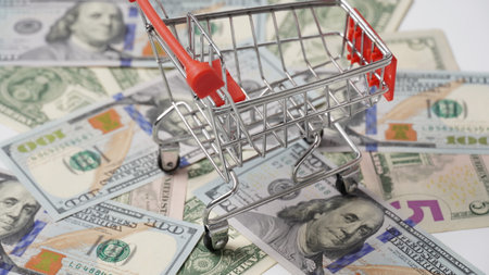 Shopping trolley above money background. Dollars cash banknotes